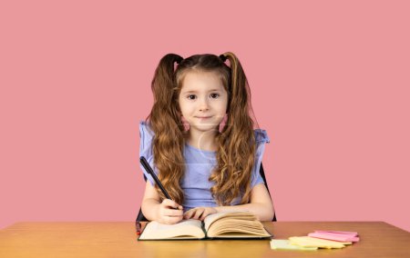 Foto de La imagen de una niña pequeña con dos coletas en el pelo y es muy hermosa, la niña se representa mientras estaba escribiendo sus deberes y preparándose para las lecciones. A la chica le gusta la escuela. - Imagen libre de derechos