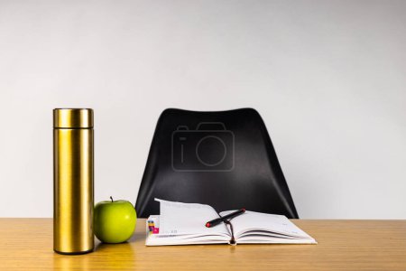 Un bureau en bois franc avec un rectangle, une pomme rouge, un thermos cylindrique et un stylo noir. Fournitures et ustensiles de bureau placés sur une table en bois