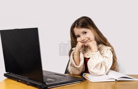 Foto de Una niña está sonriendo y sentada en un escritorio con una computadora portátil. Ella está usando sus dedos para hacer un gesto en el dispositivo de salida - Imagen libre de derechos
