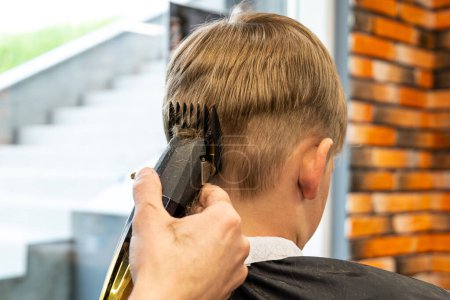 Foto de Imagen de un proceso de corte de cabello con un profesional que sostiene una máquina de corte de cabello especial, el niño tiene el cabello rubio y es pecoso. Foto de alta calidad - Imagen libre de derechos