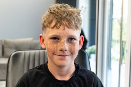 A picture of a very happy child after being cut in a barbshop salon, he has a very nice cut and has freckles on his face. High quality photo