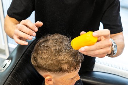 Foto de Peluquero profesional que utiliza talco en polvo para el cabello de su cliente sentado en una silla de barbero sobre fondo negro. Foto de alta calidad - Imagen libre de derechos