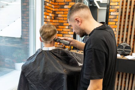 Picture of a milling process in a barbershop studio, a blond boy with blue eyes and freckles is very happy and will have a new style of milling. High quality photo