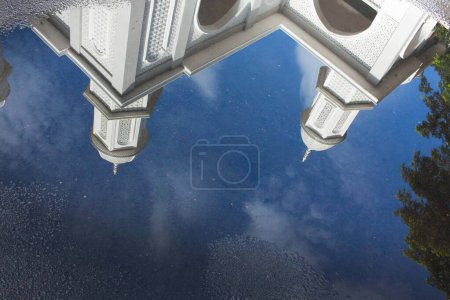 Téléchargez les photos : Vue de la mosquée blanche avec des reflets d'eau sur la route sur un fond bleu ciel - en image libre de droit