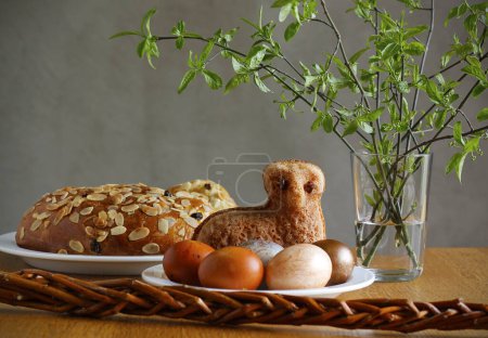 Easter still life containing a small lamb cake, painted eggs, traditional Czech Easter sweet cake called "mazanec", an Easter whip and green twigs in a vase