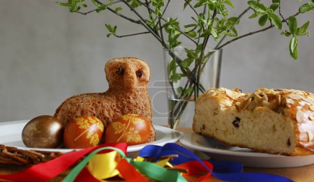Naturaleza muerta de Pascua que contiene un pequeño pastel de cordero, huevos pintados, pastel tradicional checo dulce de Pascua llamado "mazanec", un látigo de Pascua y ramitas verdes en un jarrón
