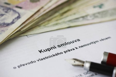 Close-up of a purchase contract on the transfer of ownership rights to real estate written in Czech language, a pack of Czech banknotes in the background. Concept for ownership, legal issues and legal documents.