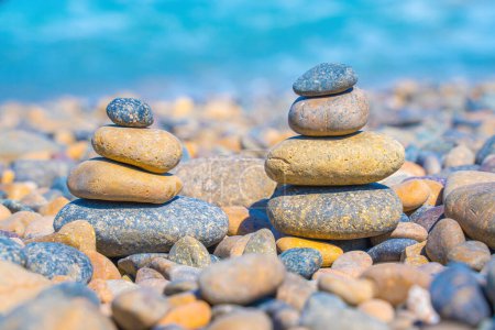 Téléchargez les photos : Symbolic scales of stones against the background of the sea and blue sky. Concept of harmony and balance. Pros and cons concept. Pyramid stones balance on the sand of the beach with blurred background - en image libre de droit