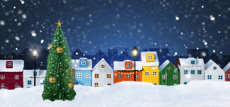 Bunte Miniaturhäuser in einer Reihe angeordnet und Weihnachtsbaum auf verschneiter Nacht Weihnachten Stadt Hintergrund. Winterliche weihnachtliche Stadtlandschaft.