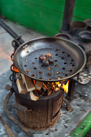 Foto de Estufa perfoforada en la que hay algunas castañas asando bajo un fuego de leña. - Imagen libre de derechos