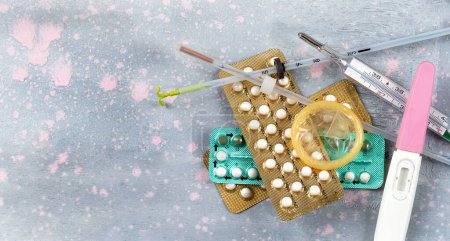 Foto de Diferentes métodos anticonceptivos vistos desde arriba sobre un fondo rosa y gris - Imagen libre de derechos