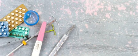 Foto de Diferentes métodos anticonceptivos vistos desde arriba sobre un fondo rosa y gris panorámico - Imagen libre de derechos