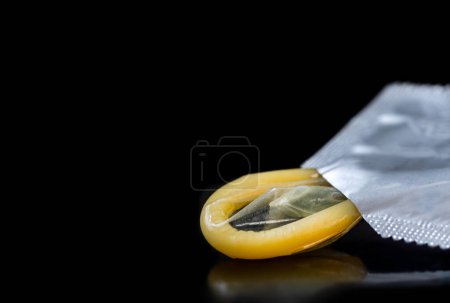 Photo for Yellow condom in horizontal plane on a black background. - Royalty Free Image