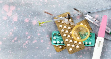 Foto de Diferentes métodos anticonceptivos vistos desde arriba sobre un fondo rosa y gris - Imagen libre de derechos