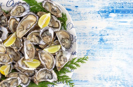 Foto de Fresh oysters with lime on a round plate. Oyster season. Seafood dish on a blue background. . - Imagen libre de derechos