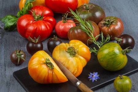 Foto de Reliquia recién cosechada y tomates de herencia en la tabla de cortar. Tomates multicolores, rojos, verdes, negros, morados, naranjas y amarillos listos para comer - Imagen libre de derechos