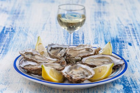 Photo for Oysters and glass of white wine in a restaurant wooden table background - Royalty Free Image