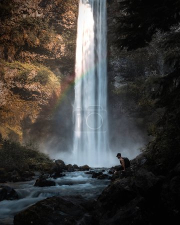 lonely man sitting by waterfall