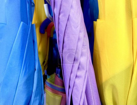 Téléchargez les photos : Rouleau de parapluie fermé bleu, violet et jaune vibrant en magasin isolé sur le ratio de photographie horizontale - en image libre de droit