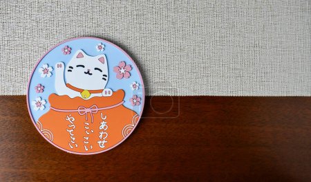 One single round drink glass coaster with maneki neko cat design isolated on horizontal kitchen table place mat and wooden table surface with copy space background.