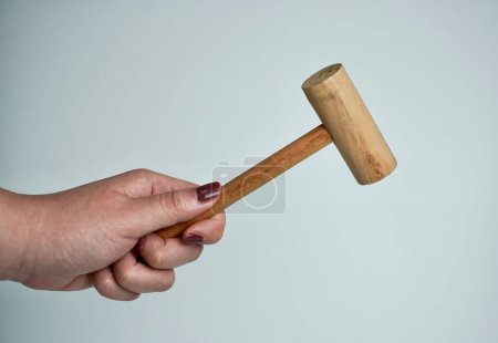 Hand mit braunem Nagellack hält Holzhammer Objektfotografie isoliert auf horizontalem Verhältnis einfachen weißen oder hellgrauen Hintergrund.