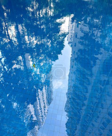 Blaues frisches Schwimmbadwasser mit Bodenfliesen und Bäumen Gebäude und Himmel Reflexion isoliert auf vertikalem Verhältnis Hintergrund.