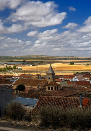 Photo for An old Spanish village among the golden fields of Castilla La Mancha on a sunny day with rich blue skies and white fluffy clouds - Royalty Free Image