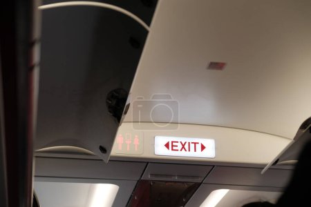 Téléchargez les photos : Un regard intérieur sur la partie supérieure d'un avion, avec le panneau omniprésent de sortie, symbole des mesures de sécurité dans le transport aérien. - en image libre de droit