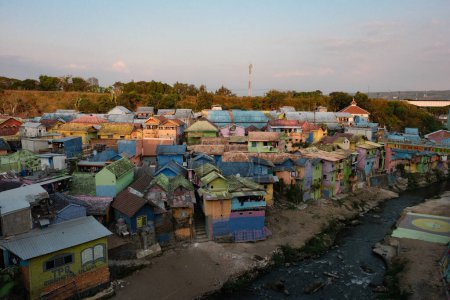 Téléchargez les photos : Explorez les couleurs enchanteresses de Jodipan, Malang, tandis que les maisons ornées de teintes vives bordent la rivière sereine. Cette scène de village pittoresque témoigne de l'esprit artistique - en image libre de droit