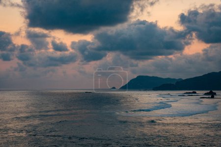 Foto de Experimenta la magia del crepúsculo mientras el sol se despide, pintando el cielo en tonos de nubes azules oscuras y tonos amarillentos. En Bukit Merese, Lombok, la naturaleza desvela un espectáculo impresionante - Imagen libre de derechos