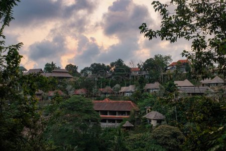 Foto de Experimente la encantadora hora dorada en Ubud, Indonesia, donde el sol arroja un cálido resplandor amarillento, iluminando las casas ubicadas en medio de exuberantes árboles. - Imagen libre de derechos