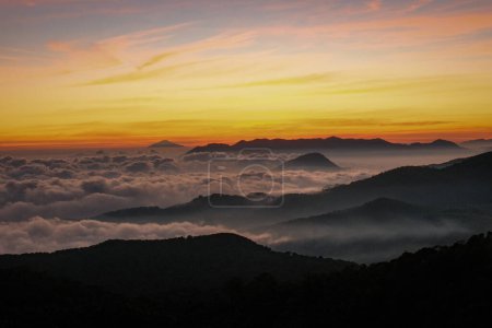 Foto de Sea testigo de la enigmática belleza de Kawah Putih mientras las nubes giran misteriosamente alrededor de los picos. El cielo se transforma de naranja vibrante a azul rosado etéreo - Imagen libre de derechos