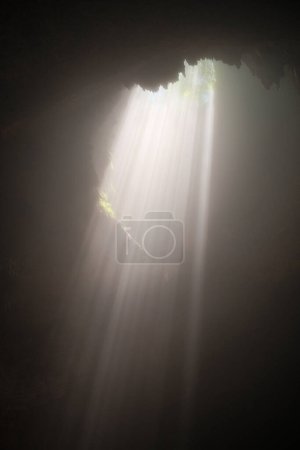 Foto de Contempla el encanto celestial mientras los rayos de luz radiantes adornan el interior de Cave Jomblang, creando un tapiz celestial en las profundidades subterráneas. - Imagen libre de derechos