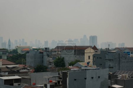 Téléchargez les photos : Assistez à la tapisserie urbaine de Jakarta : bâtiments de la classe moyenne, fermes et fiers, juxtaposés à des gratte-ciel brumeux, symboles de richesse au loin. - en image libre de droit
