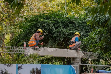 Téléchargez les photos : Dédié travailleurs indonésiens de la construction sur un pieu de béton, martelant avec détermination dans un contexte d'arbres, symbolisant le progrès et le travail acharné. - en image libre de droit