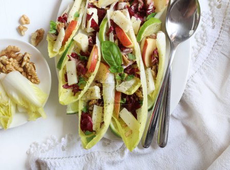 Photo for Endive leaves stuffed with cheese, walnuts, apple, radishes, honey and lime sprinkled with fresh basil leaves. Directly above. - Royalty Free Image