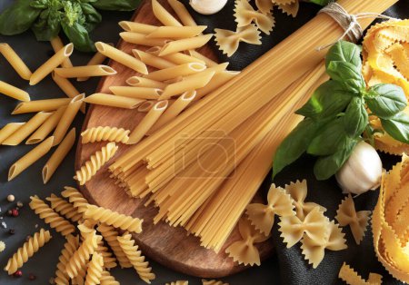 Verschiedene Arten italienischer Pasta mit Gemüse und Kräutern auf grauem Hintergrund. Aus der Vogelperspektive. Kochkonzept. Kopierraum.