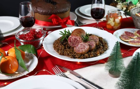 Photo for Traditional Italian Christmas food. Cotechino with lentils, appetizer, fruits, red wine and Panettone. Family gathering concept. Overhead view. - Royalty Free Image