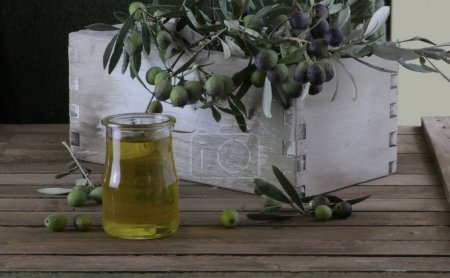 Téléchargez les photos : Branches d'olivier dans une boîte en bois et un verre avec de l'huile d'olive fraîche. Concept culinaire italien. Gros plan. - en image libre de droit