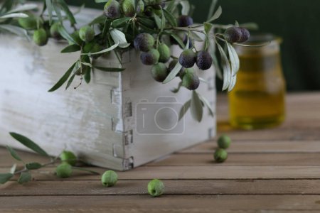 Téléchargez les photos : Branches d'olivier dans une boîte en bois et huile d'olive en arrière-plan flou. Concept culinaire italien. Gros plan. - en image libre de droit
