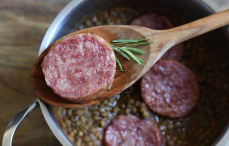 Photo for New Year's Eve meal Italian style. A slices of cotechino (pork sausage), lentils and rosemary on spoon, blurred background. Overhead view, close-up. Holiday season. - Royalty Free Image