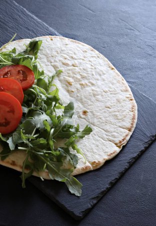Photo for Traditional Italian piadina with ham, cheese, rocked salad and tomatoes isolated on black background. Italian food street. Overhead view. Copy space. - Royalty Free Image
