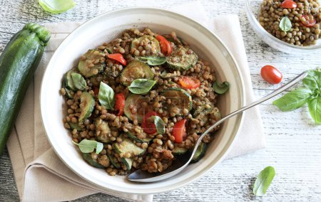 Lentils with courgettes and cherry tomatoes flavored with basil leaves, side dish or second course on a white background. Vegan food. Directly above.