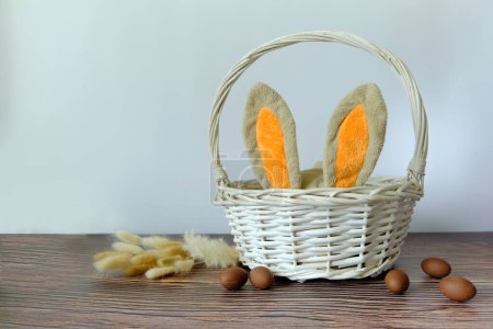 Téléchargez les photos : Oeufs de Pâques et un panier blanc avec des oreilles de lapin - en image libre de droit