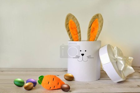 Téléchargez les photos : Oreilles de lapin de Pâques dans une boîte cadeau avec carotte sur fond en bois - en image libre de droit