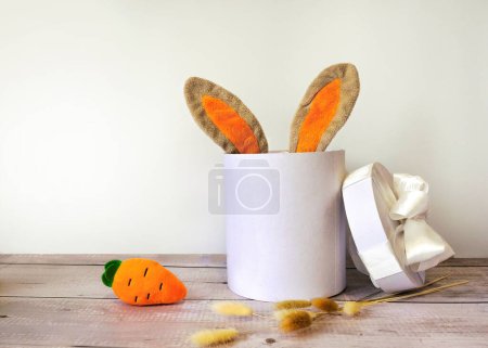 Téléchargez les photos : Oreilles de lapin de Pâques dans une boîte cadeau avec carotte sur fond en bois - en image libre de droit
