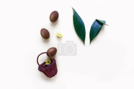Téléchargez les photos : Oeufs de Pâques en chocolat dans le panier avec des oreilles de lapin de feuilles - en image libre de droit