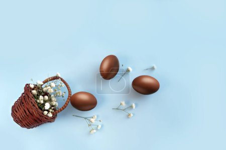 Téléchargez les photos : Oeufs de Pâques chocolat avec des fleurs dans le panier sur fond bleu - en image libre de droit