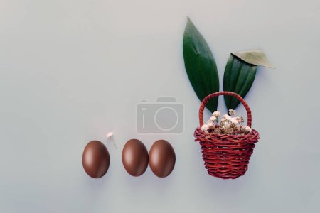 Téléchargez les photos : Oeufs de Pâques chocolat avec des fleurs dans le panier sur fond bleu - en image libre de droit