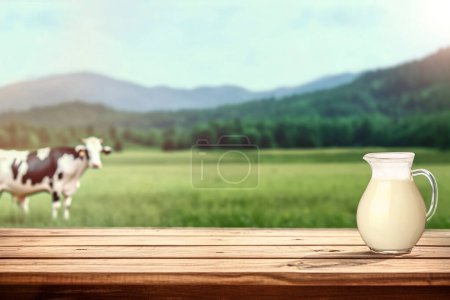 Téléchargez les photos : Lait frais sur table rustique en face d'un fond de campagne flou avec vache sur prairie - en image libre de droit